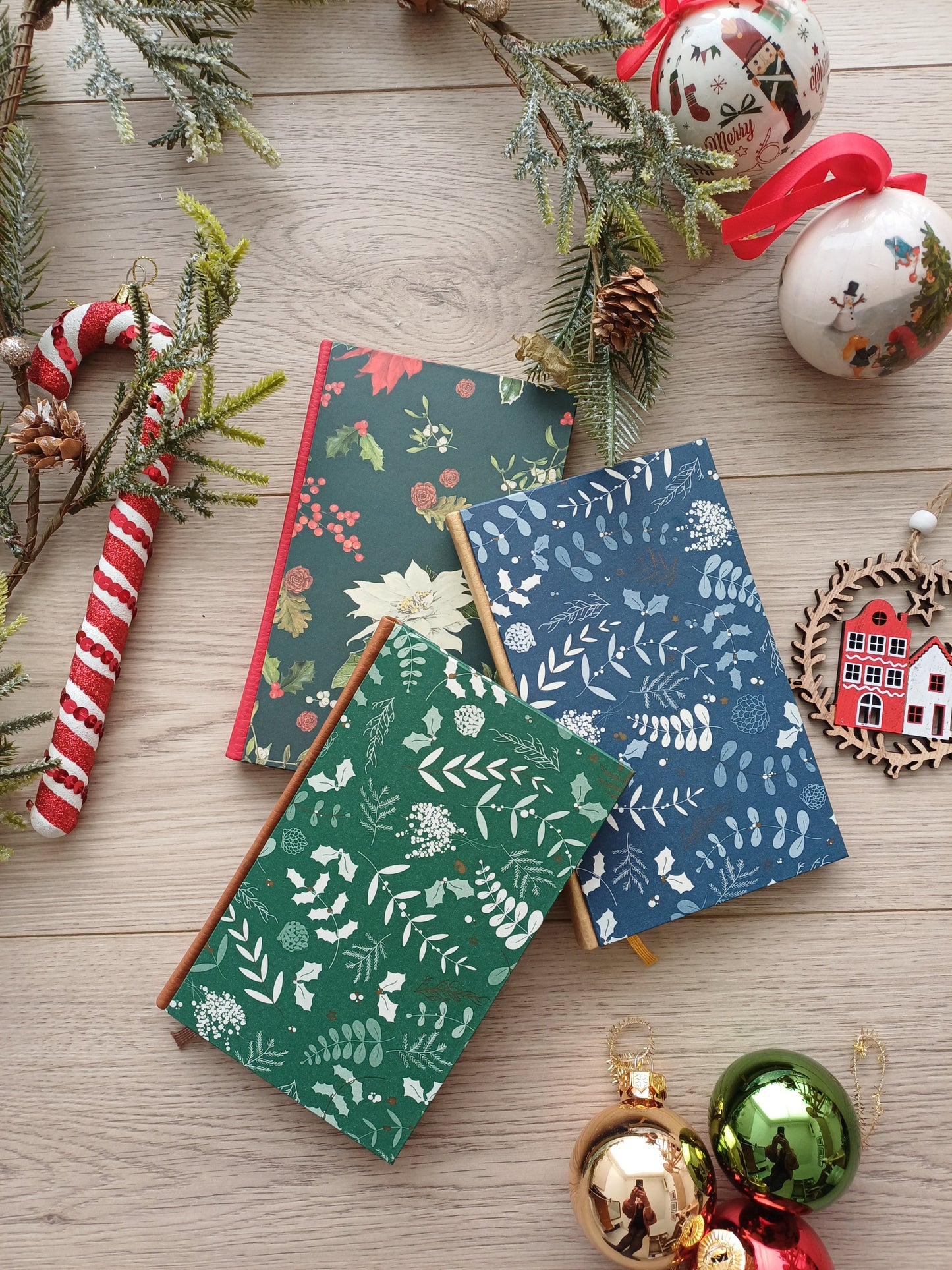 Trois carnets superposés avec des couvertures aux feuillages de Noël entourés de décorations de Noël.
