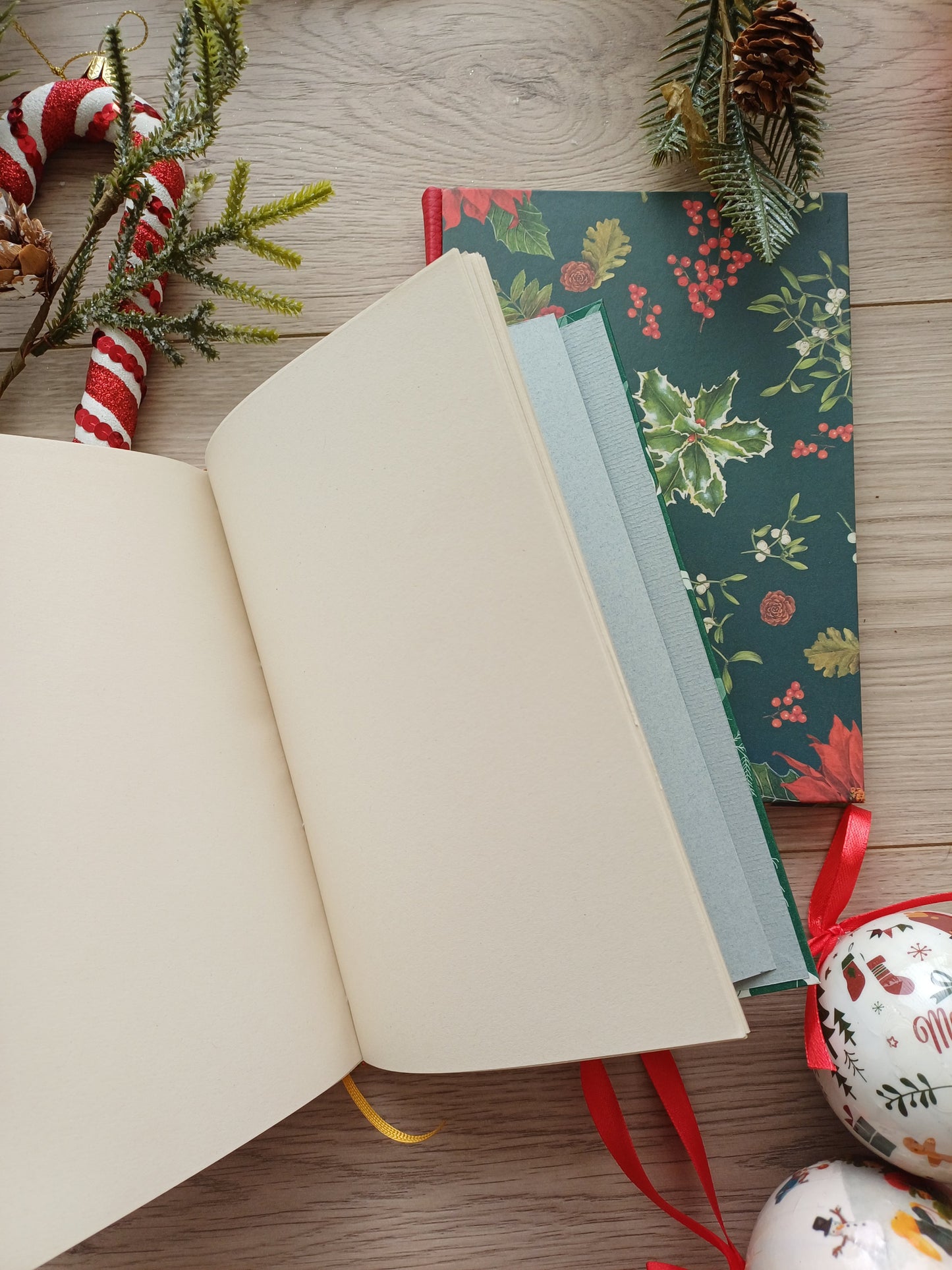 Deux carnets aux couvertures de Noël dont un est ouvert sur des pages blanches, entourés de décorations de Noël.