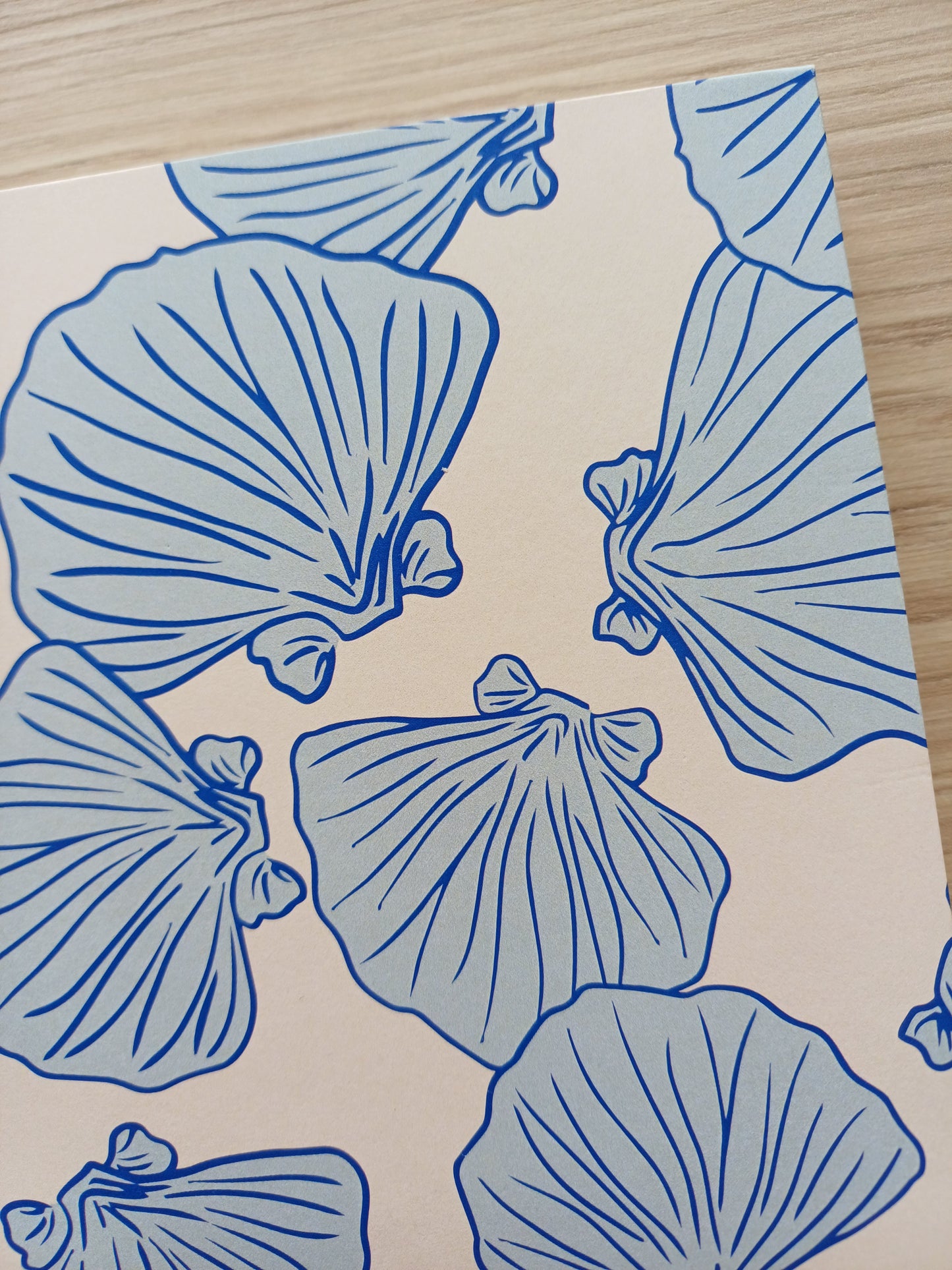 Détail de la couverture d'un carnet artisanal pour aquarelle avec des motifs de coquillages bleus sur un fond beige.