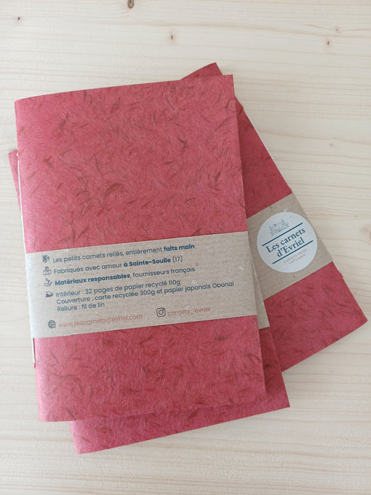 Petit carnet artisanal à la couverture de papier japonais obonai de couleur terracotta. Il est entouré d'un bandeau de papier kreft avec la composition du carnet.