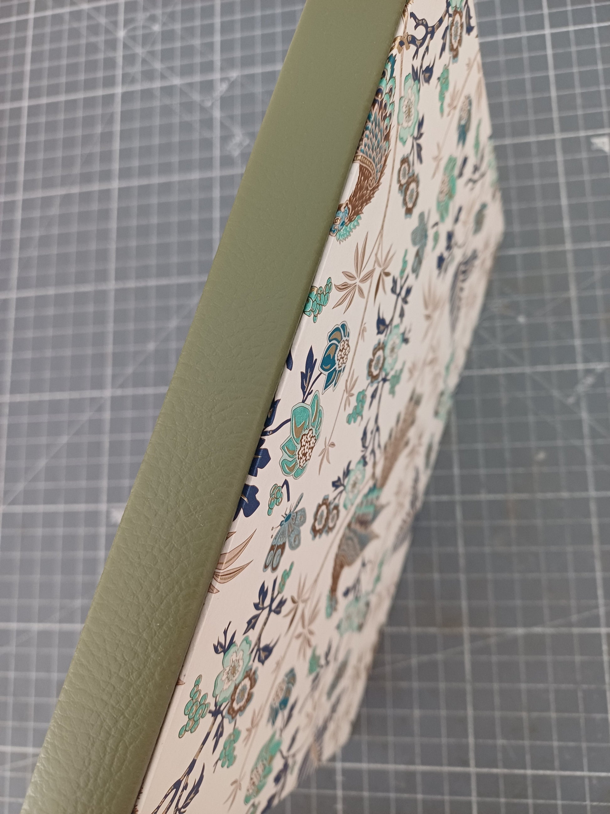 Carnet artisanal à la couverture imprimée de paons et de végétation aux reflets dorés avec un gros plan sur le dos en similicuir vert.