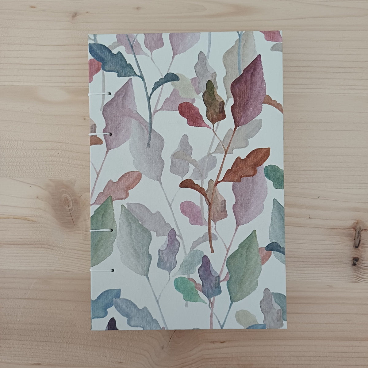 Carnet artisanal relié fermé sur la couverture au papier imprimé de feuilles d'automne.