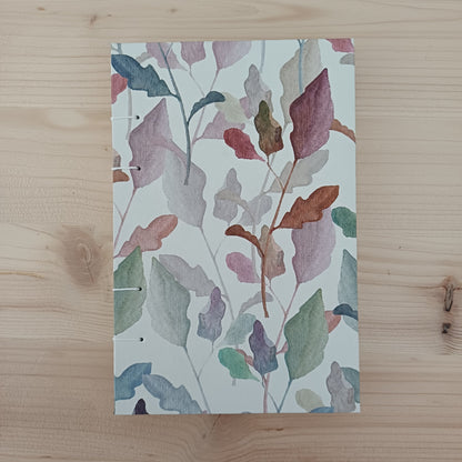 Carnet artisanal relié fermé sur la couverture au papier imprimé de feuilles d'automne.