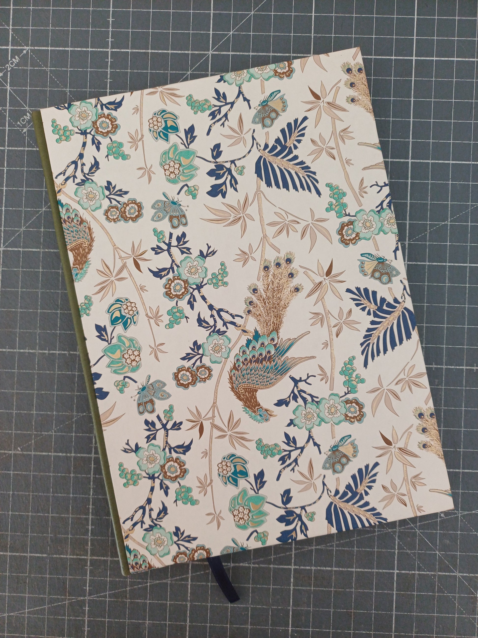 Carnet artisanal à la couverture imprimée de paons et de végétation aux reflets dorés avec un dos en similicuir vert.