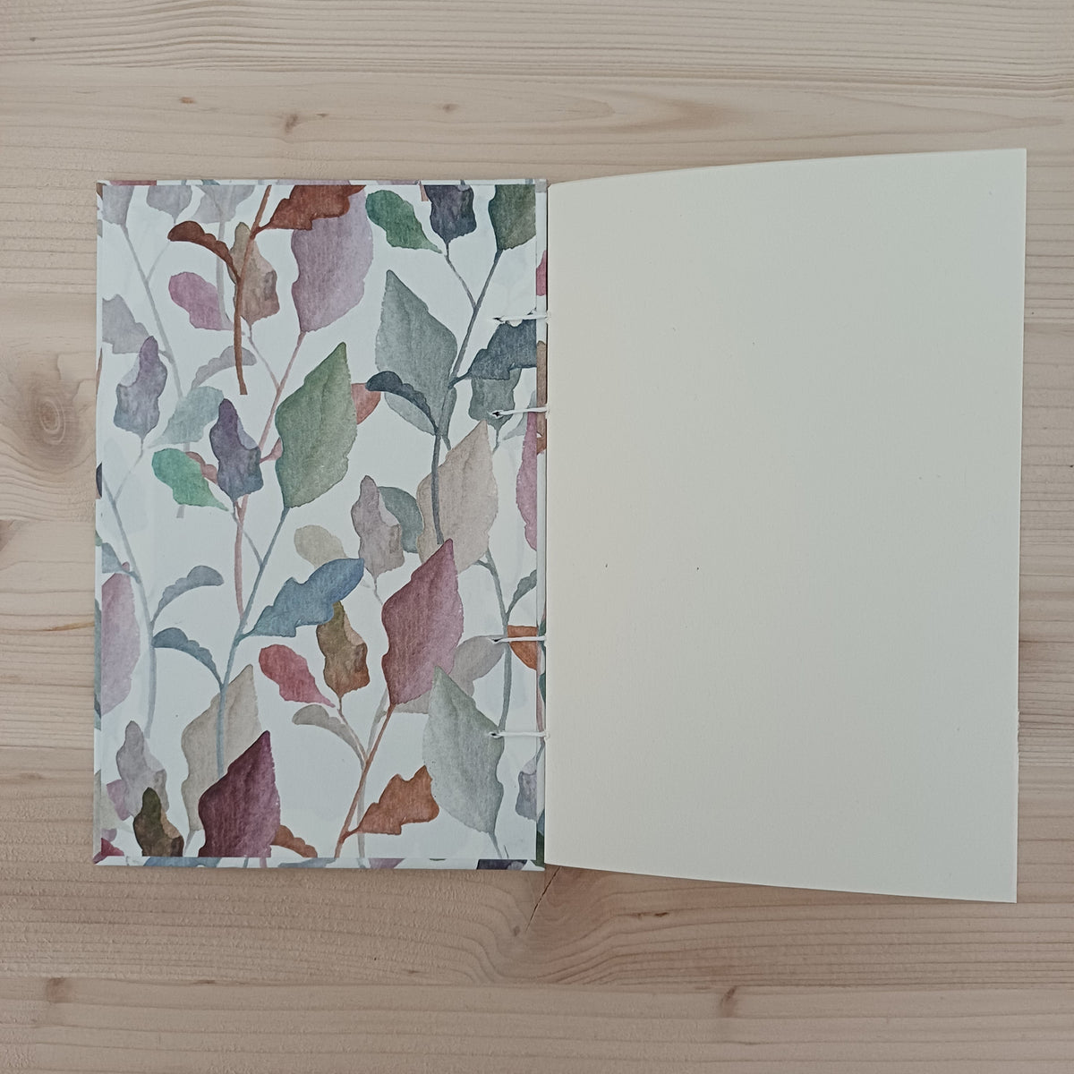Carnet artisanal relié ouvert sur la première page laissant voir l'intérieur de la couverture au papier imprimé de feuilles d'automne
