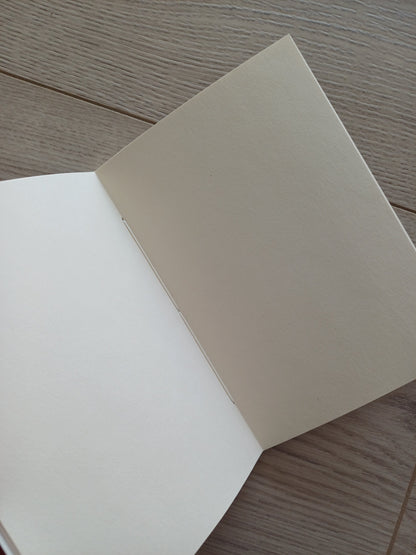 Carnet artisanal ouvert sur sa reliure qu'on voit entre les pages.