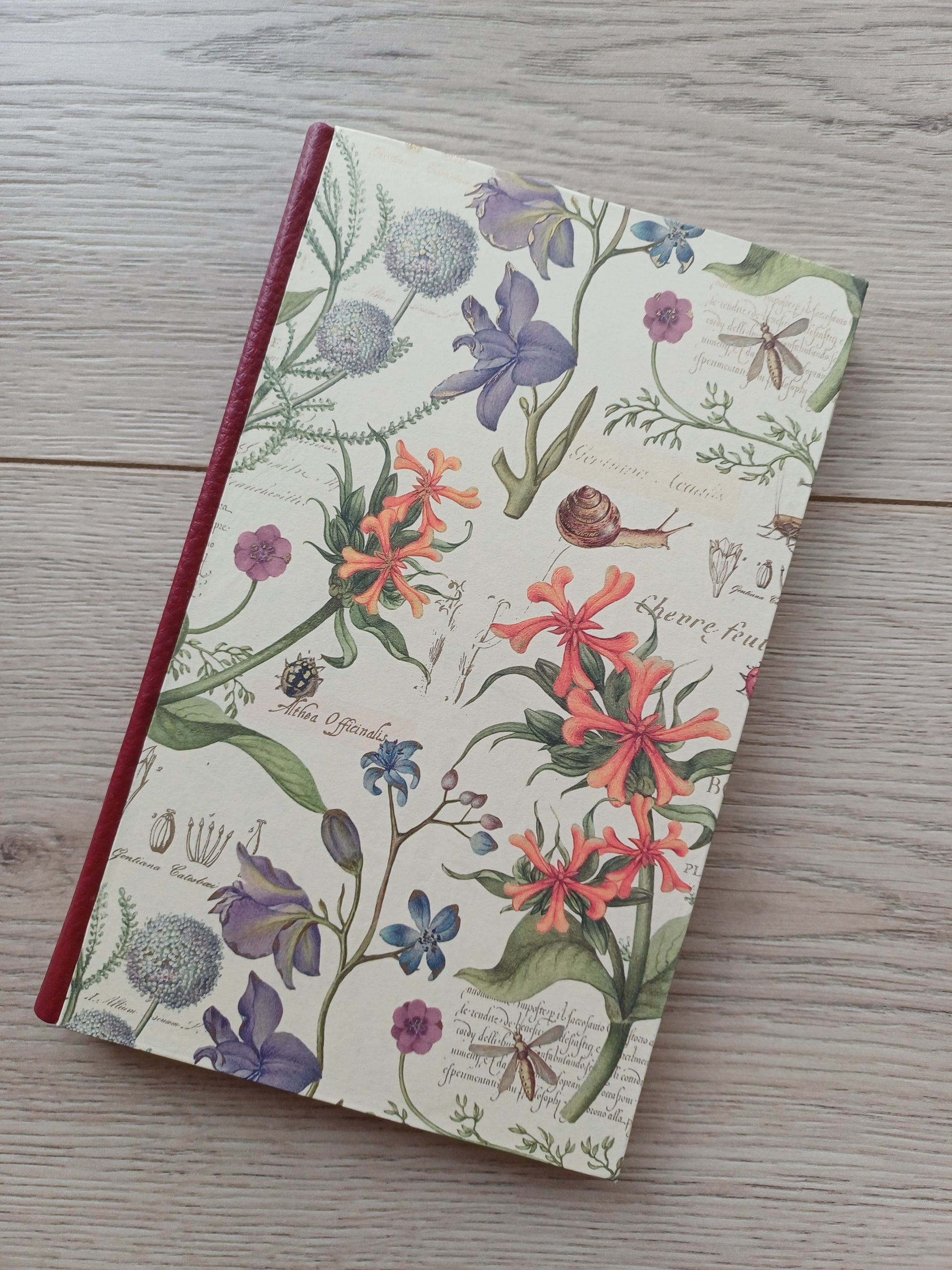 Carnet artisanal avec une couverture imprimée de fleurs, d'insectes et de notes au style cahier de botanique.