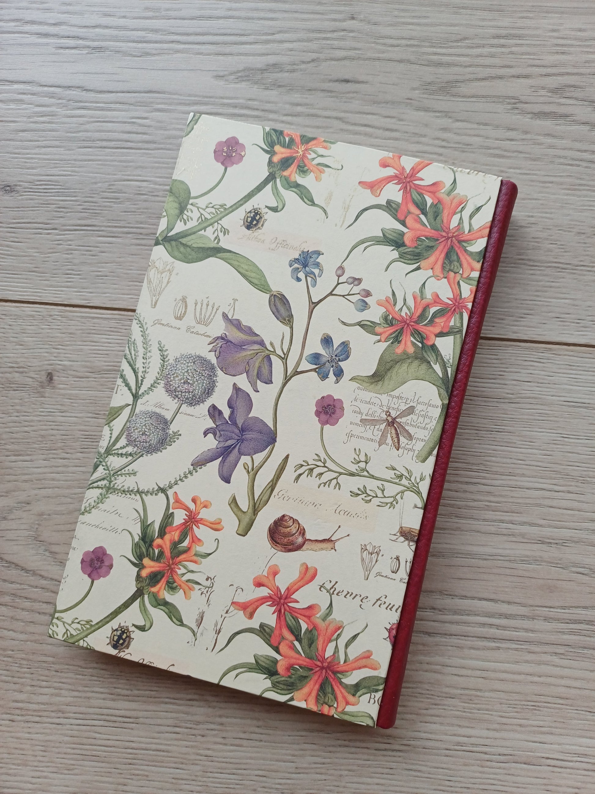 Carnet artisanal avec une couverture imprimée de fleurs, d'insectes et de notes au style cahier de botanique.