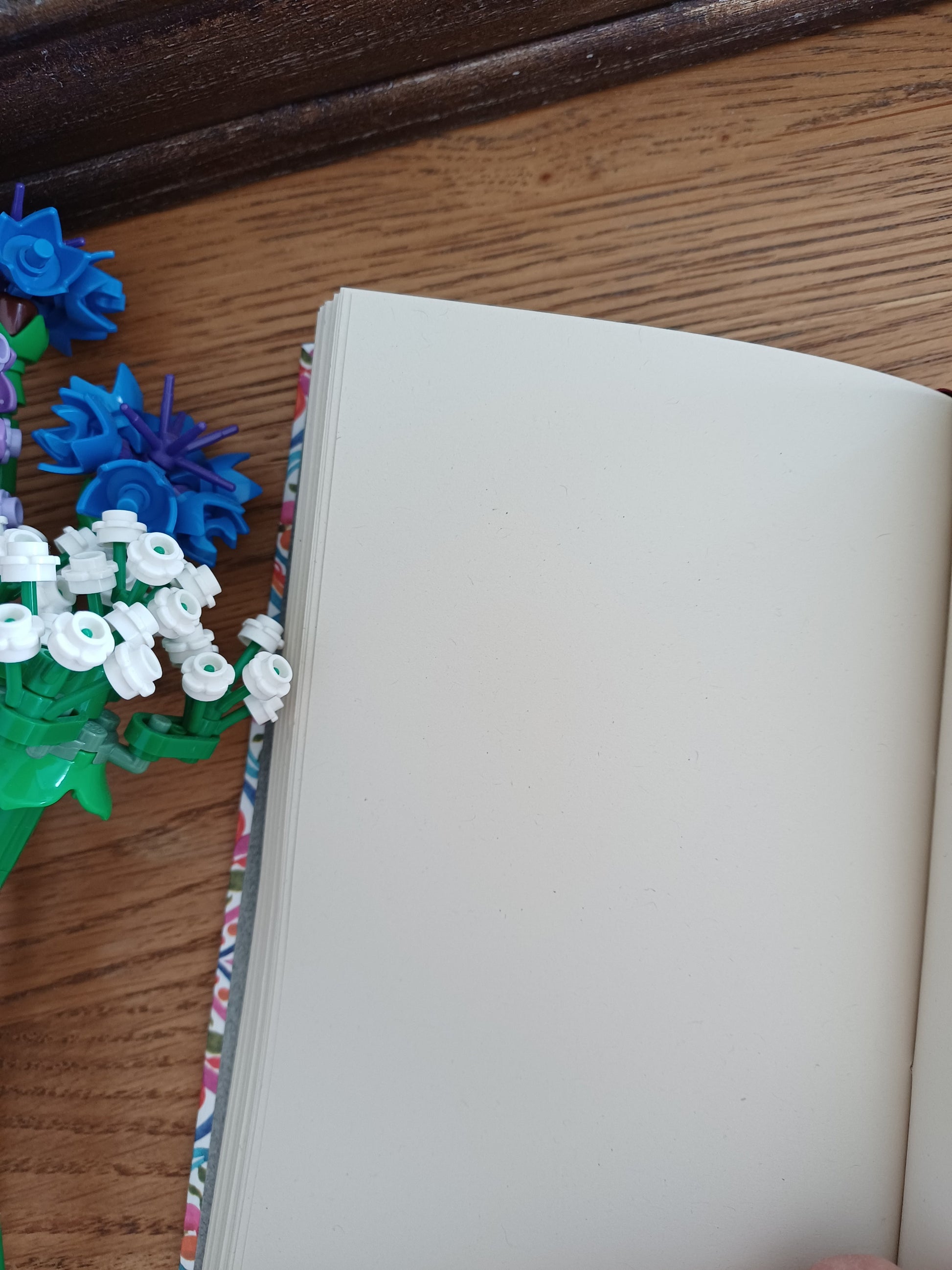 Carnet artisanal ouvert sur une page blanche à coté de fleurs en legos.