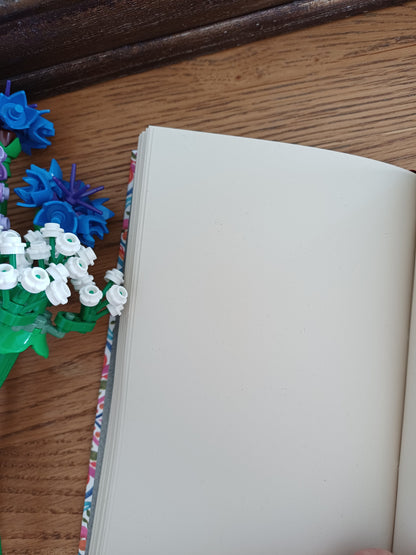 Carnet artisanal ouvert sur une page blanche à coté de fleurs en legos.
