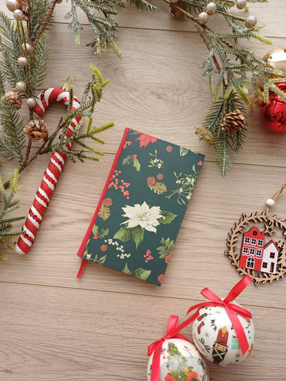 Carnet à la couverture évoquant Noël avec des fleurs et feuillages festifs entouré de décorations de Noël.