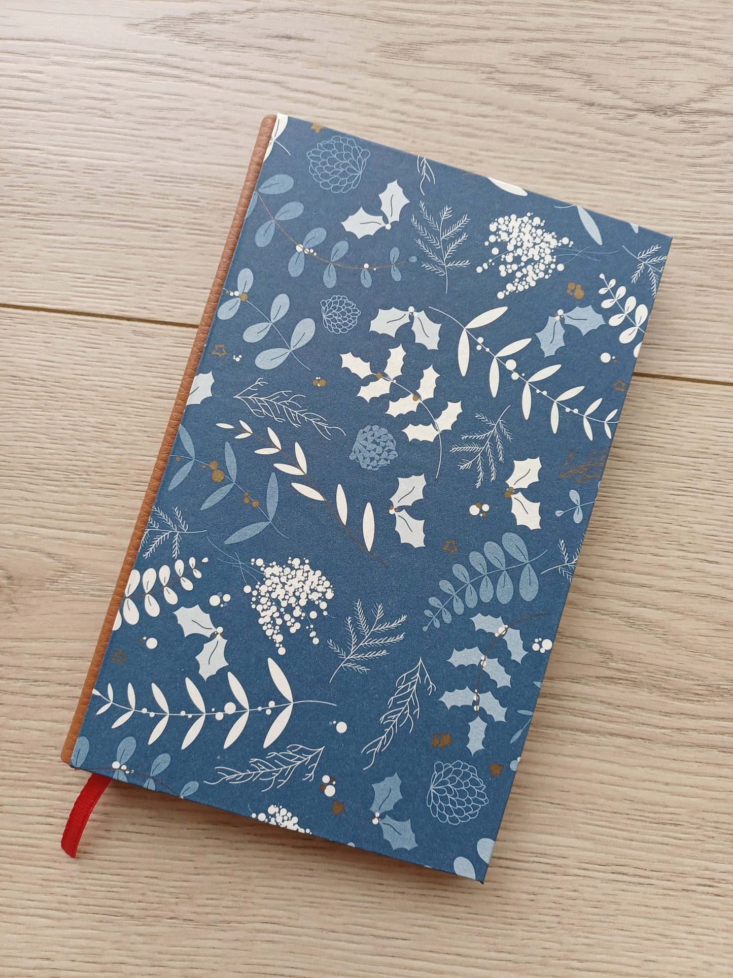 Carnet artisanal avec une couverture imprimée de motifs végétaux rappelant Noël sur fond bleu.