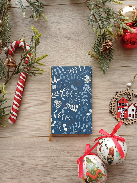 Carnet à la couverture bleu avec des feuillages évoquant Noël entouré de décorations de Noël.