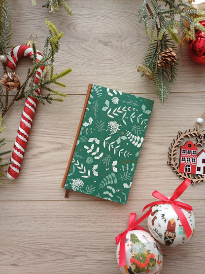 Carnet aux feuillages de Noël sur fond vert entouré de décorations de Noël