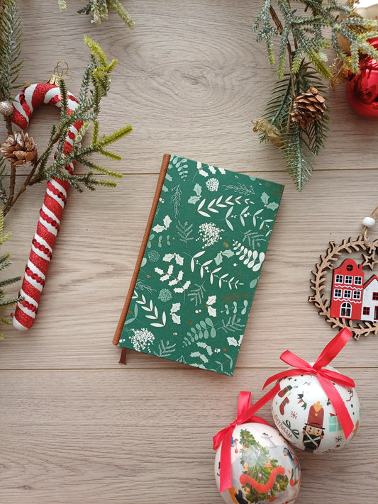Carnet aux feuillages de Noël sur fond vert entouré de décorations de Noël