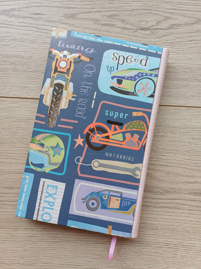 Carnet artisanal avec une couverture imprimée de dessins évoquant les roads trips et la route 66 : des voitures, des motos, des panneaux...