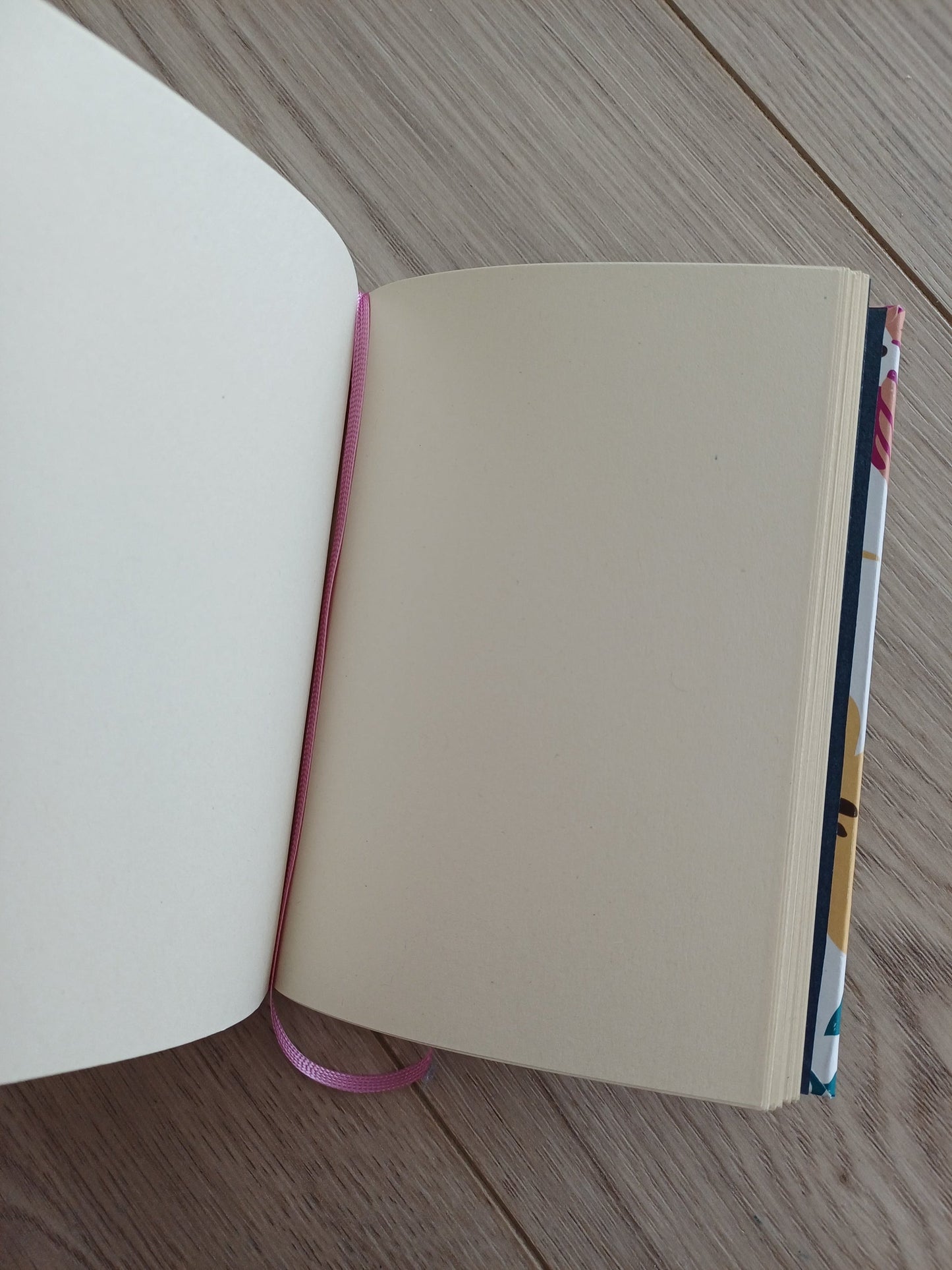Carnet artisanal ouvert, on voit le signet rose et un bout de couverture au papier imprimé fleuri.