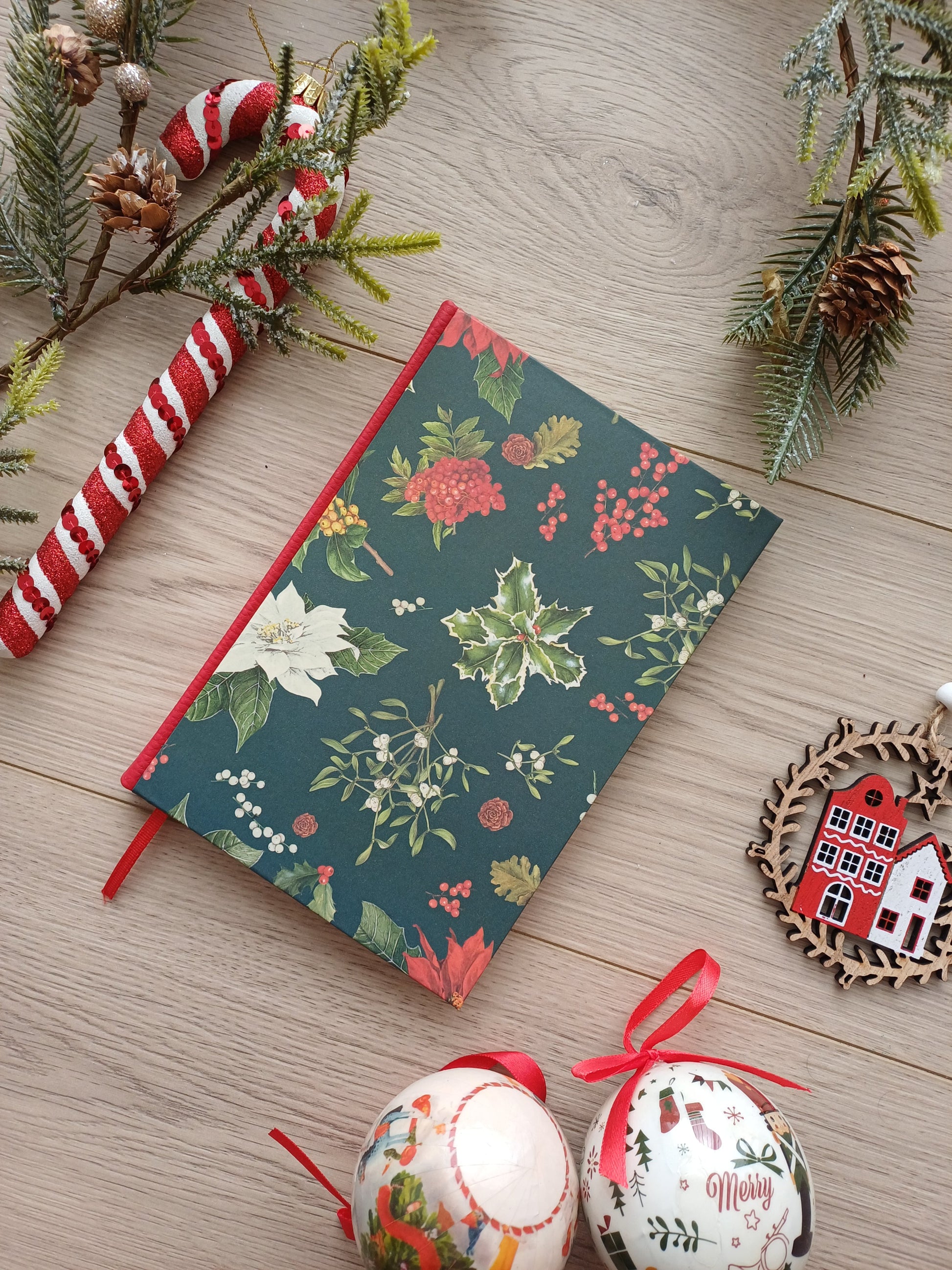 Carnet à la couverture aux feuillages de Noël entouré de décorations de Noël.