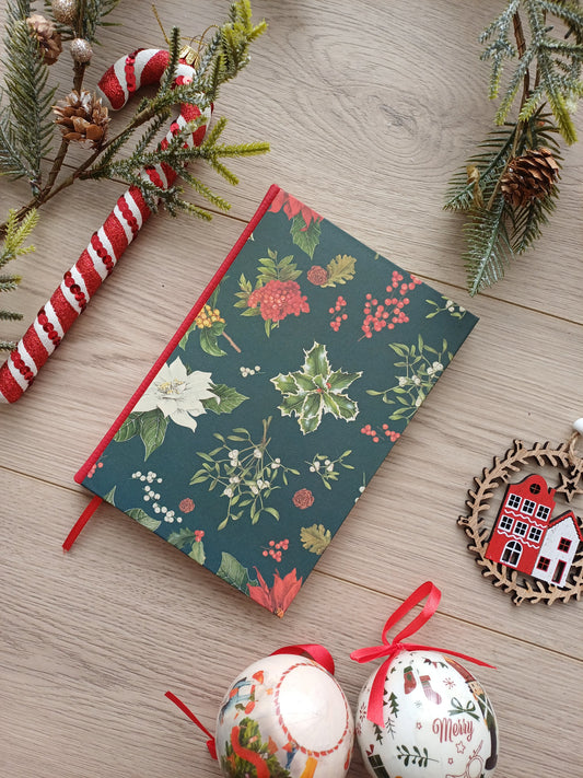 Carnet à la couverture aux feuillages de Noël entouré de décorations de Noël.