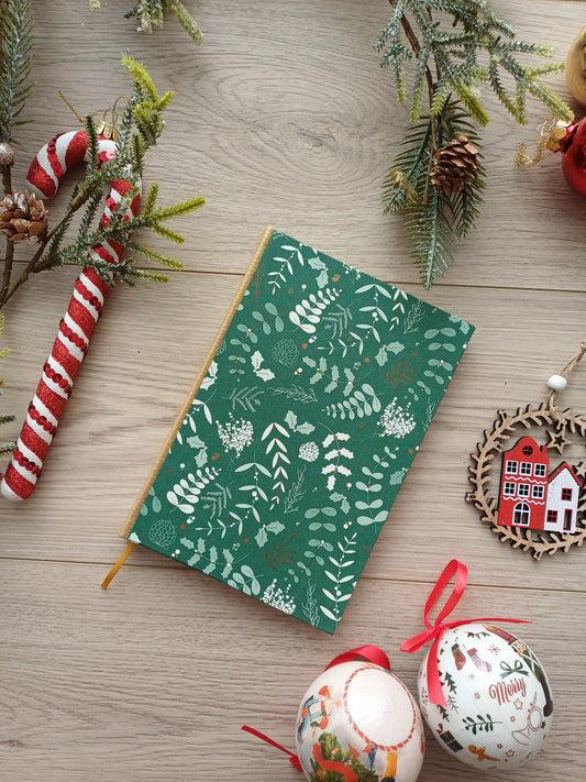 Carnet aux allures de Noël avec des feuillages sur fond vert entouré de décorations de Noël.