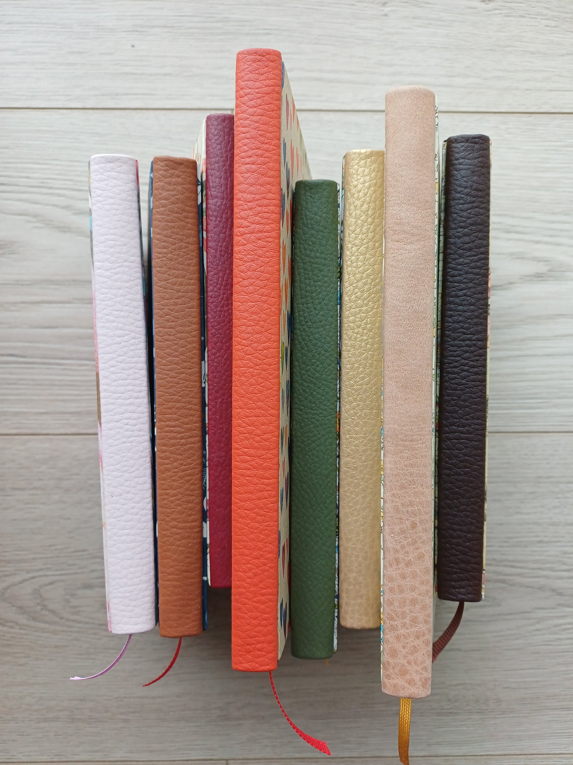 Huit carnets alignés dont on ne voit que le dos en faux cuir, tous de différentes couleurs.