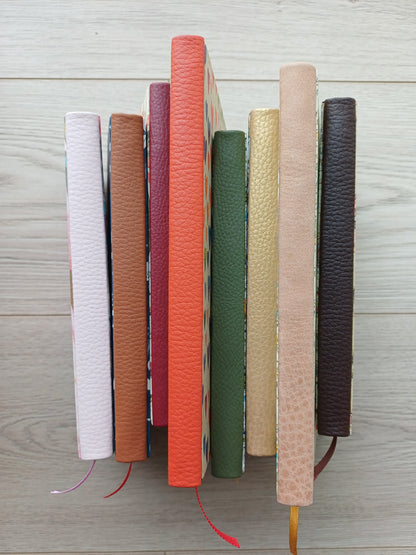Huit carnets alignés dont on ne voit que le dos en faux cuir, tous de différentes couleurs.