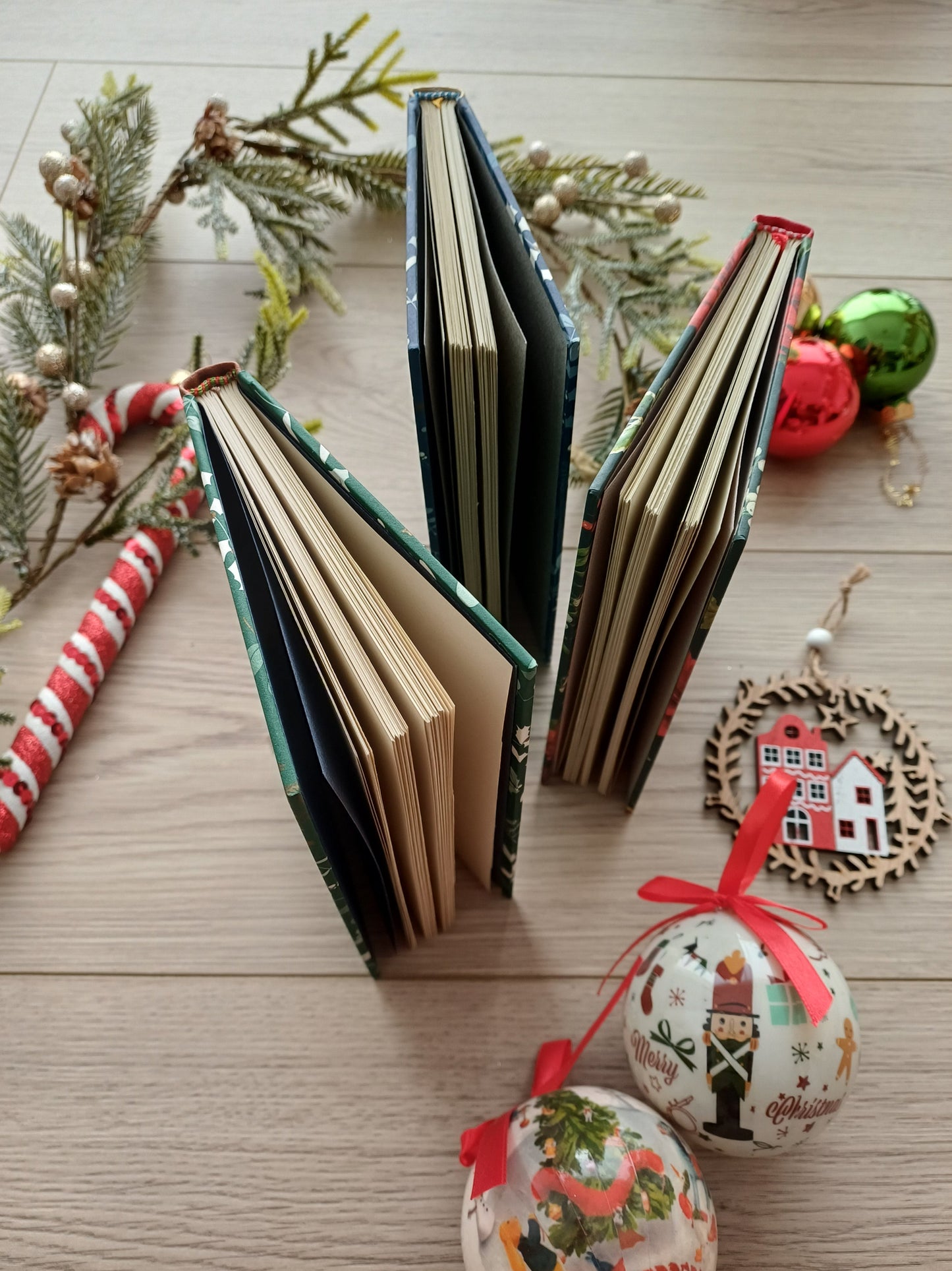 Trois carnets aux couvertures de Noël posés debout et entrouverts entourés de décoration de Noël.