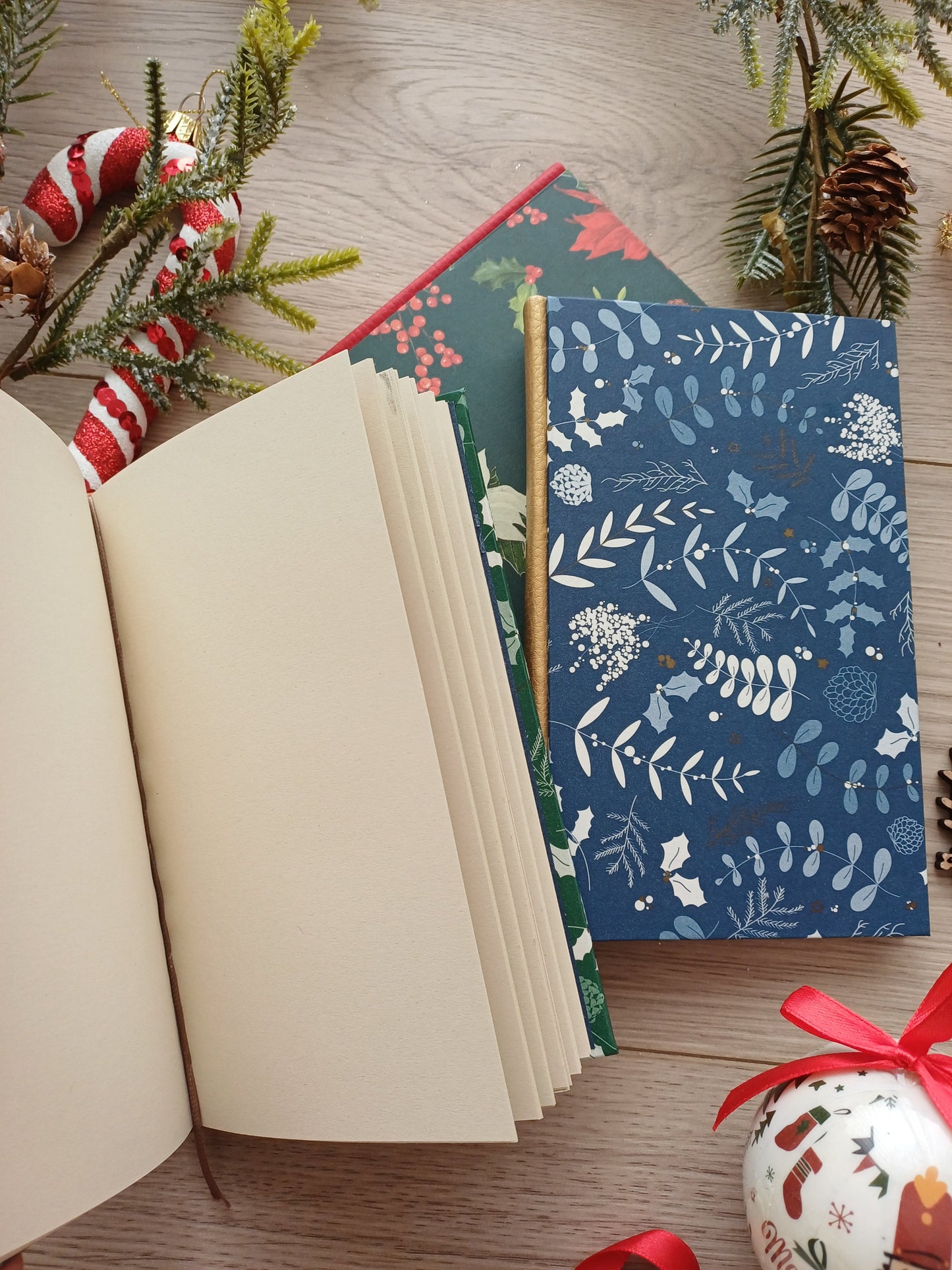 Carnets artisanaux aux motifs de Noël, fermés et ouverts entourés de décorations de Noël.