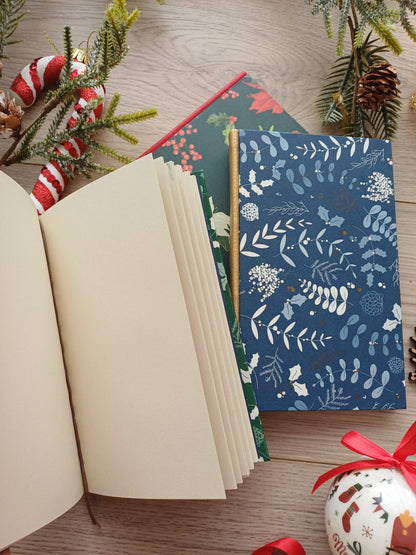 Carnets artisanaux aux motifs de Noël, fermés et ouverts entourés de décorations de Noël.