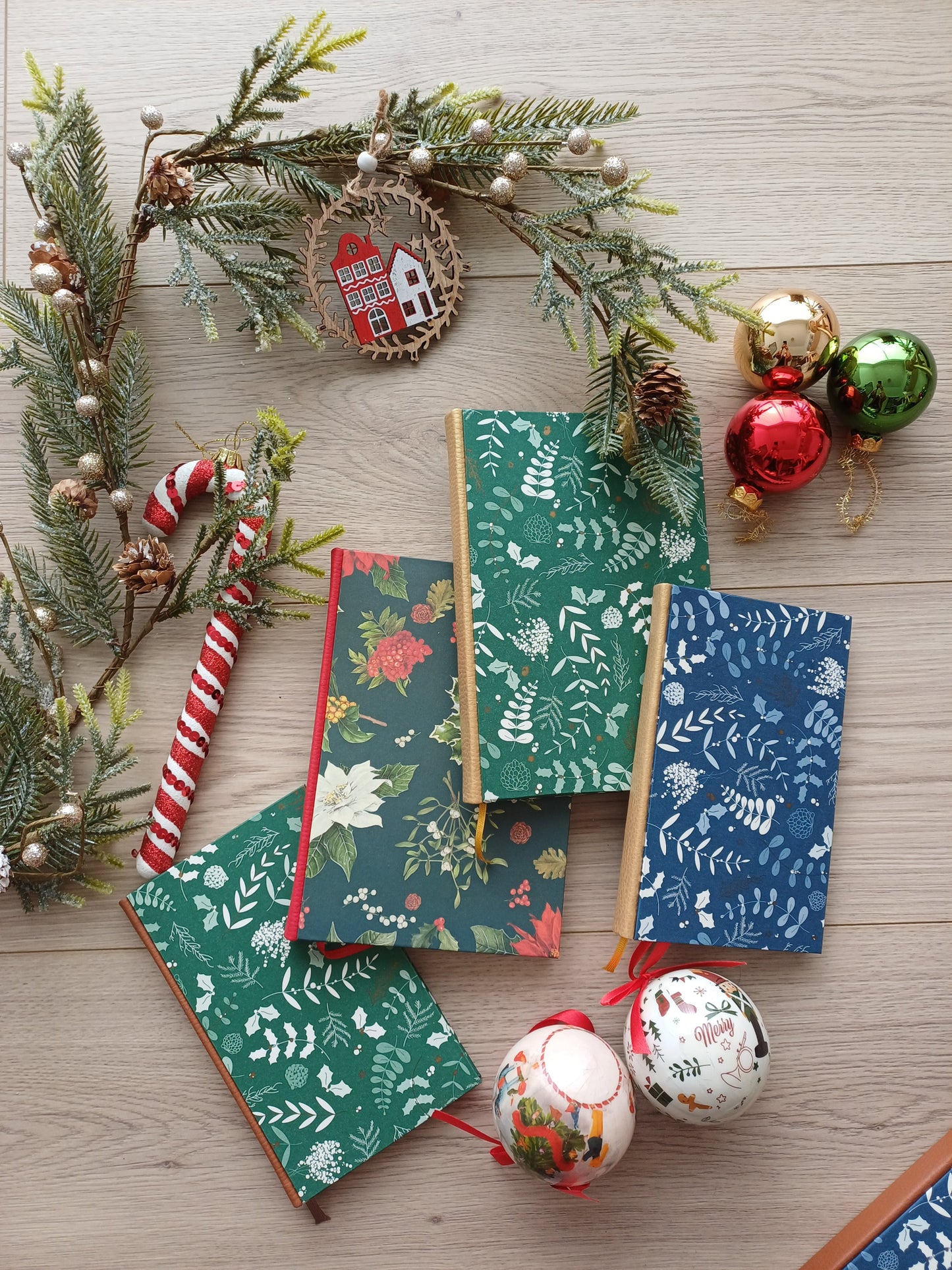 Quatre carnets de Noël aux motifs festifs entourés de décorations de Noël.