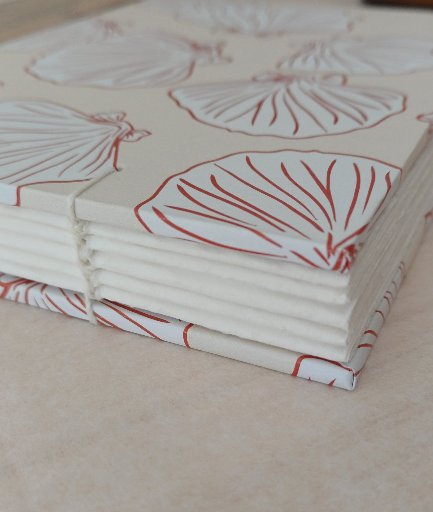 Détail d'un carnet artisanal relié en reliure copte visible. La couverture du carnet présente des motifs de coquillages de couleur beige et terracotta.