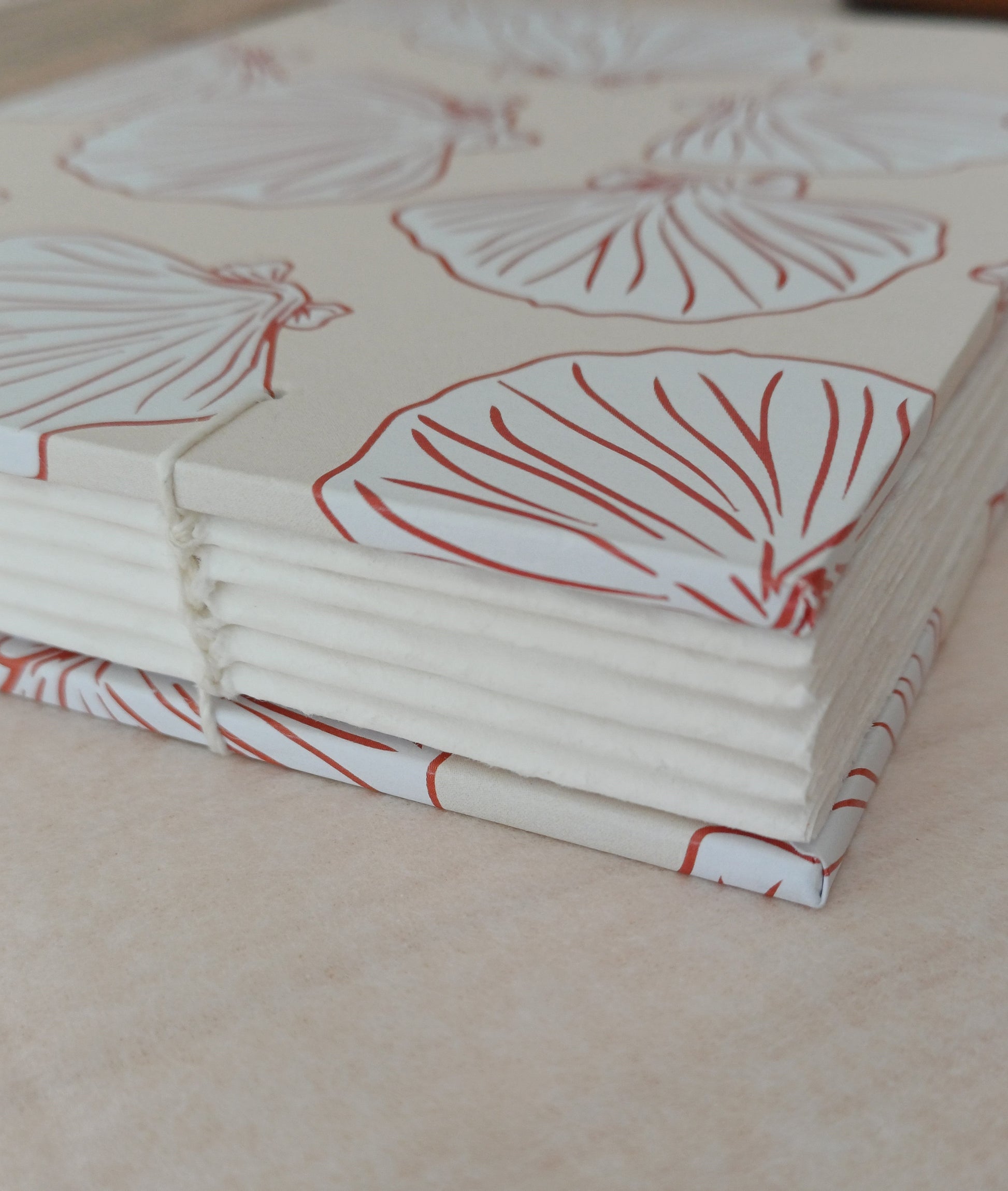 Détail d'un carnet artisanal relié en reliure copte visible. La couverture du carnet présente des motifs de coquillages de couleur beige et terracotta.
