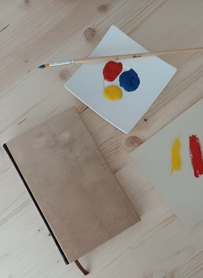Carnet à la couverture imprimé d'un papier effet bois à côté d'une palette de peinture et un pinceau.