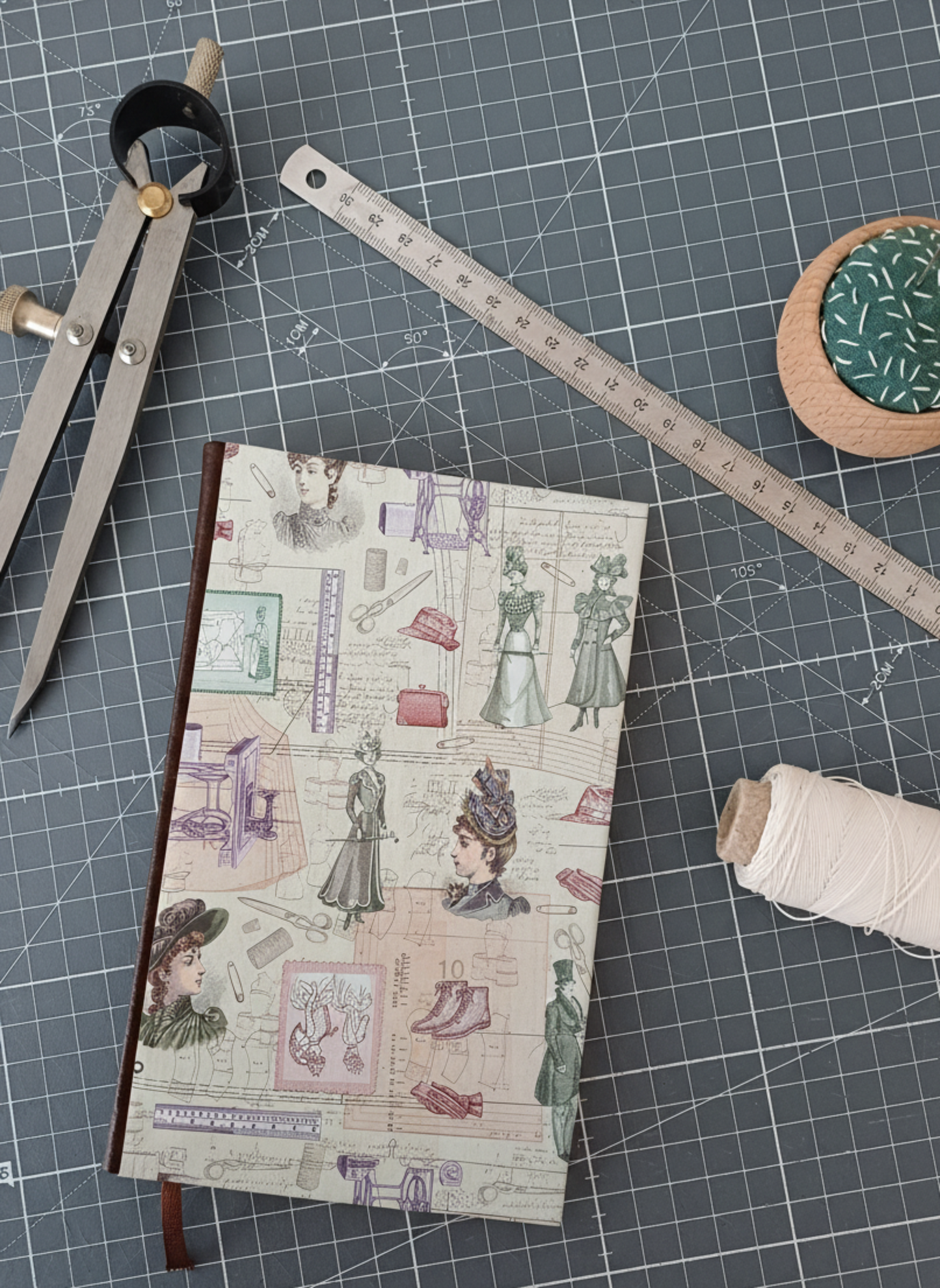Carnet à la couverture imprimée de dessin de couture, entouré d'un compas, d'un réglet d'aiguilles et de fil.