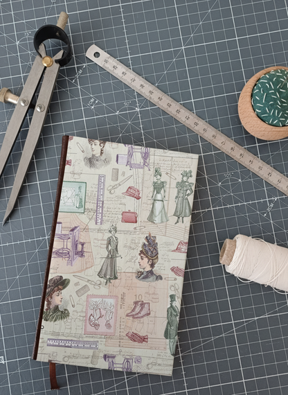 Carnet à la couverture imprimée de dessin de couture, entouré d'un compas, d'un réglet d'aiguilles et de fil.