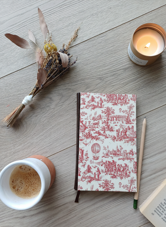 Carnet à la couverture imprimée avec des dessins vintage de toile de jouy, entouré de fleurs, d'un café, d'une bougie, d'un livre et d'un crayon.