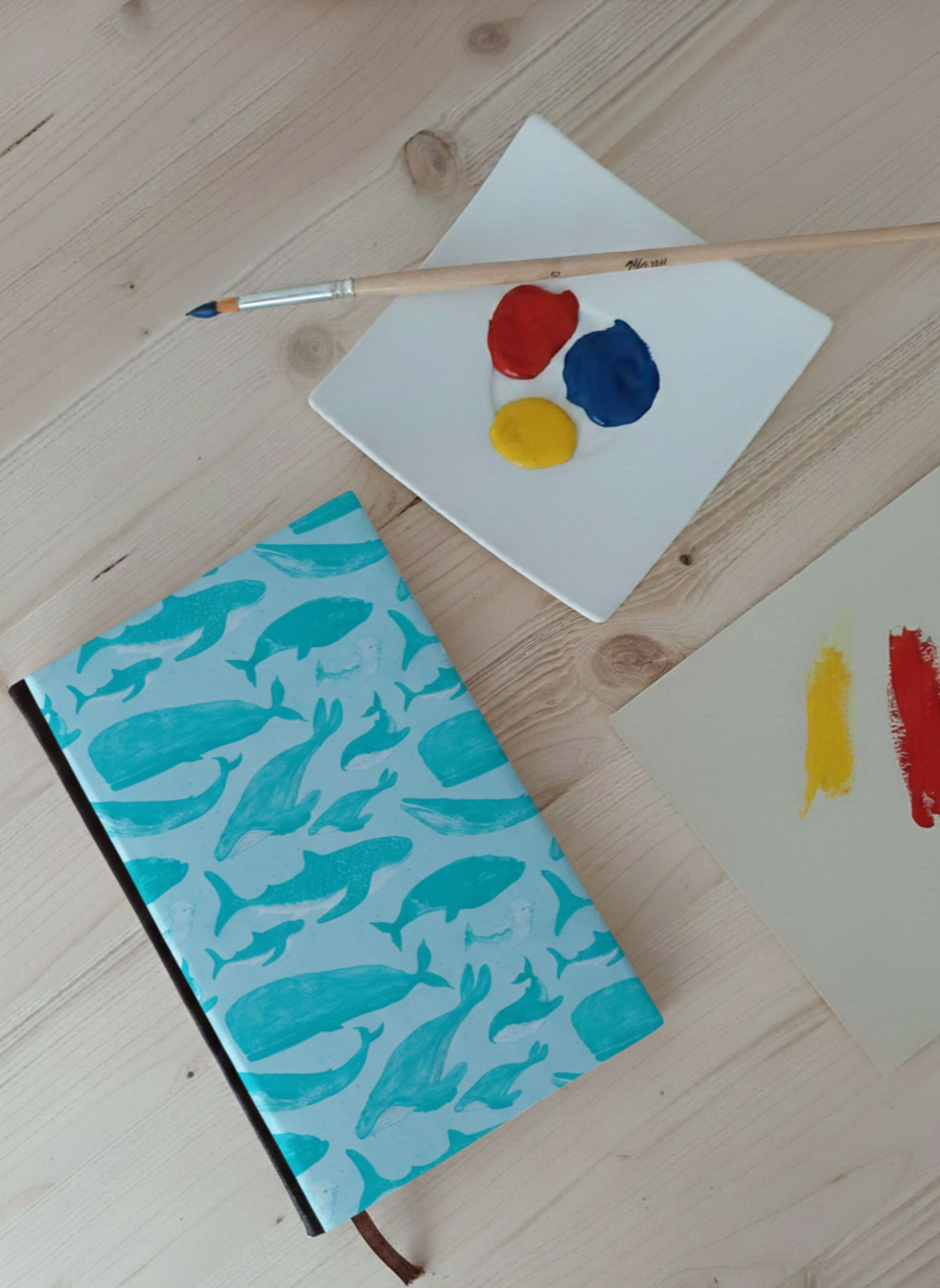 Carnet à la couverture imprimé d'un dessin de mammifères marins à côté d'une palette de peinture et un pinceau.
