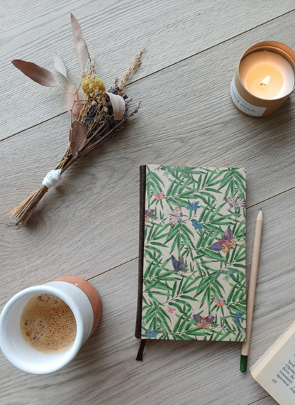 Carnet à la couverture imprimée avec des motifs marbrés dorés, entouré de fleurs, d'un café, d'une bougie, d'un livre et d'un crayon.