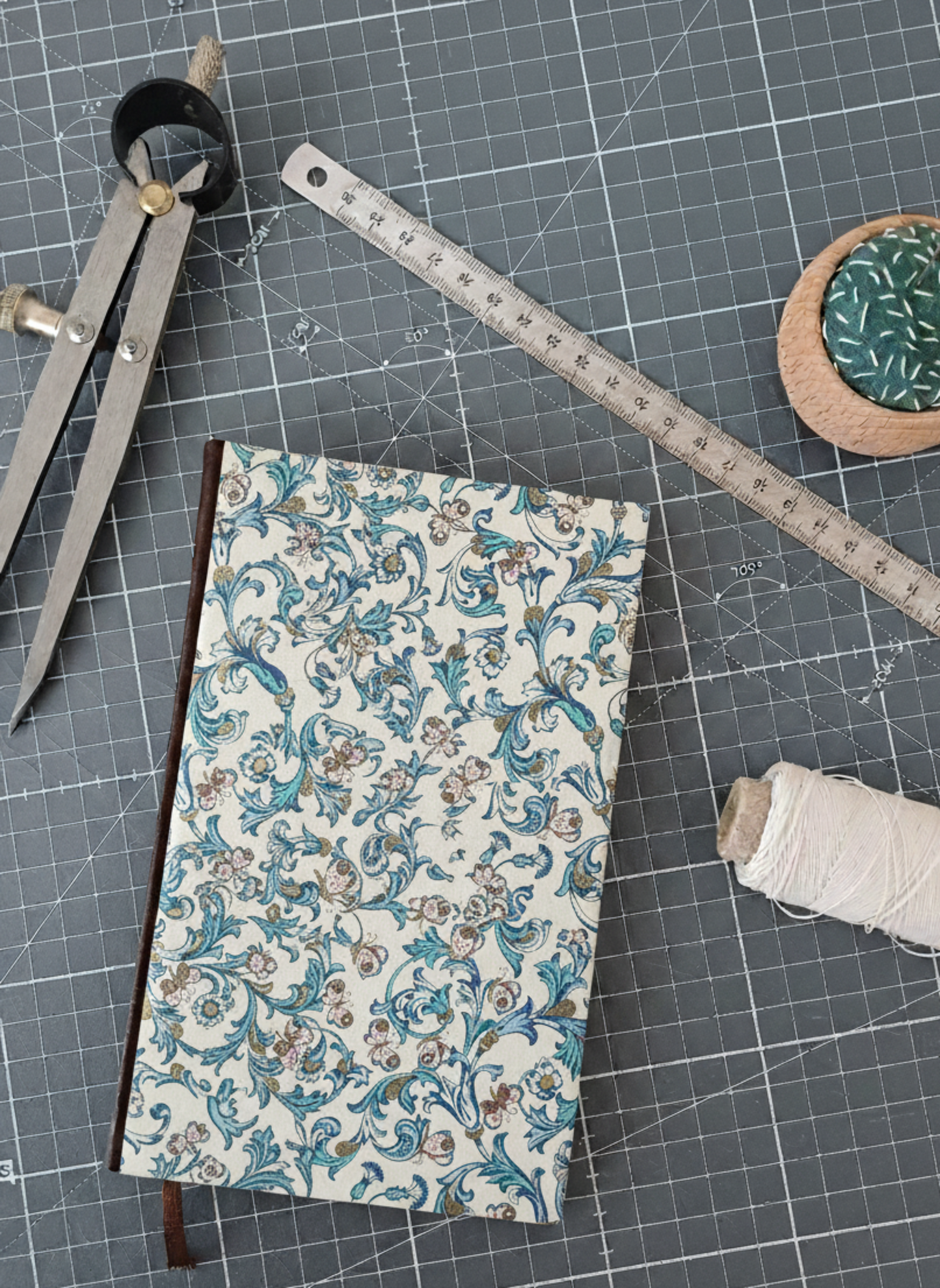 Carnet à la couverture imprimée de motifs fleuris et de papillons entouré d'un compas, d'un réglet d'aiguilles et de fil.