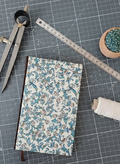 Carnet à la couverture imprimée de motifs fleuris et de papillons entouré d'un compas, d'un réglet d'aiguilles et de fil.