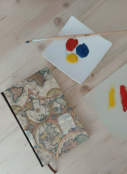 Carnet à la couverture imprimée de planisphères à côté d'une palette de peinture et un pinceau.