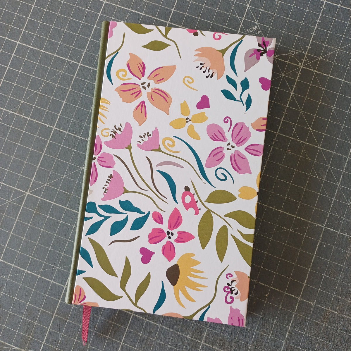 Carnet artisanal à la couverture imprimée de motifs floraux colorés, avec un dos en similicuir kaki et un signet bordeaux.
