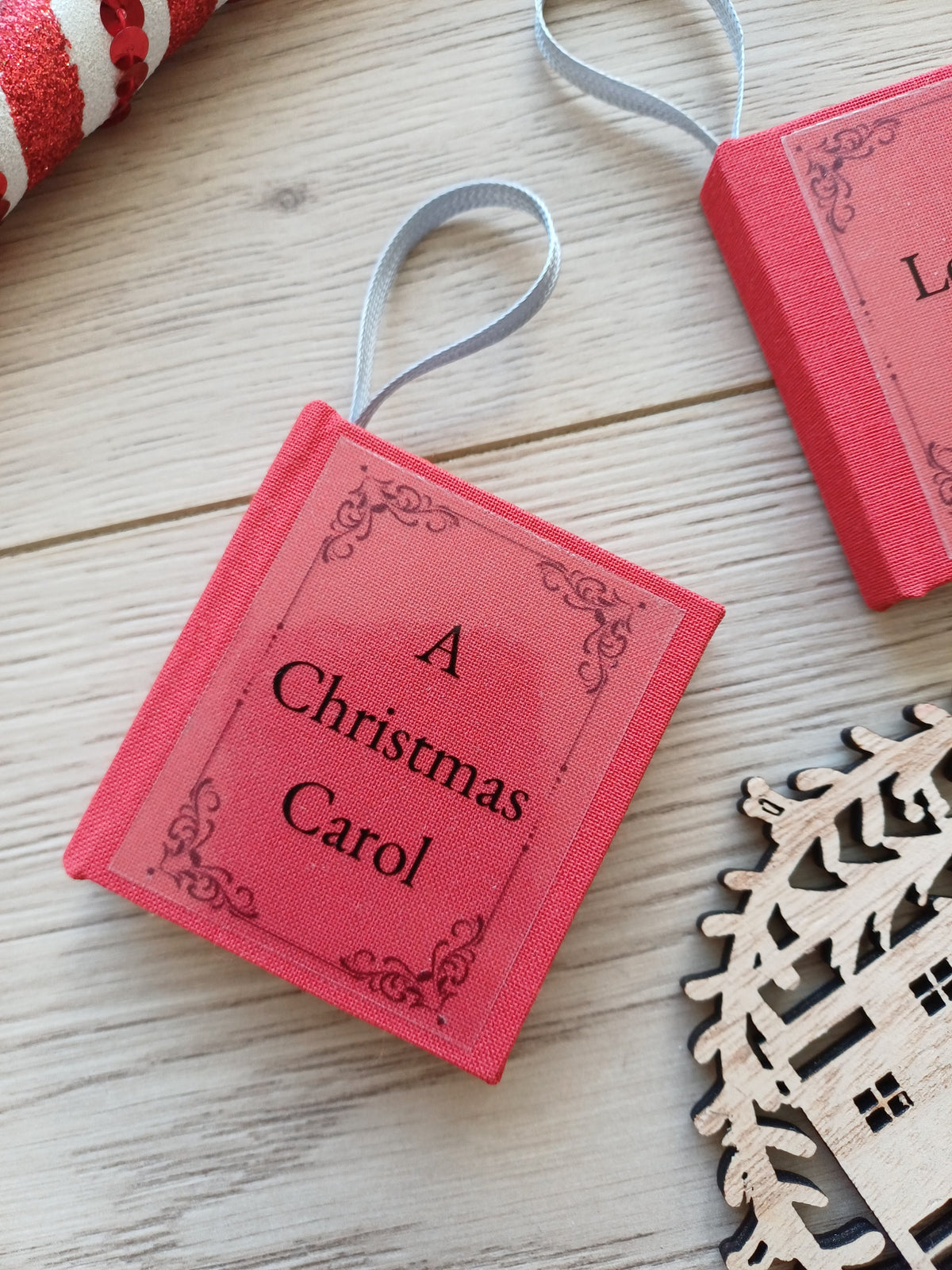 Un petit carnet rouge en forme de livre avec le tire "A Christmas Carol" entouré de décorations de Noël.