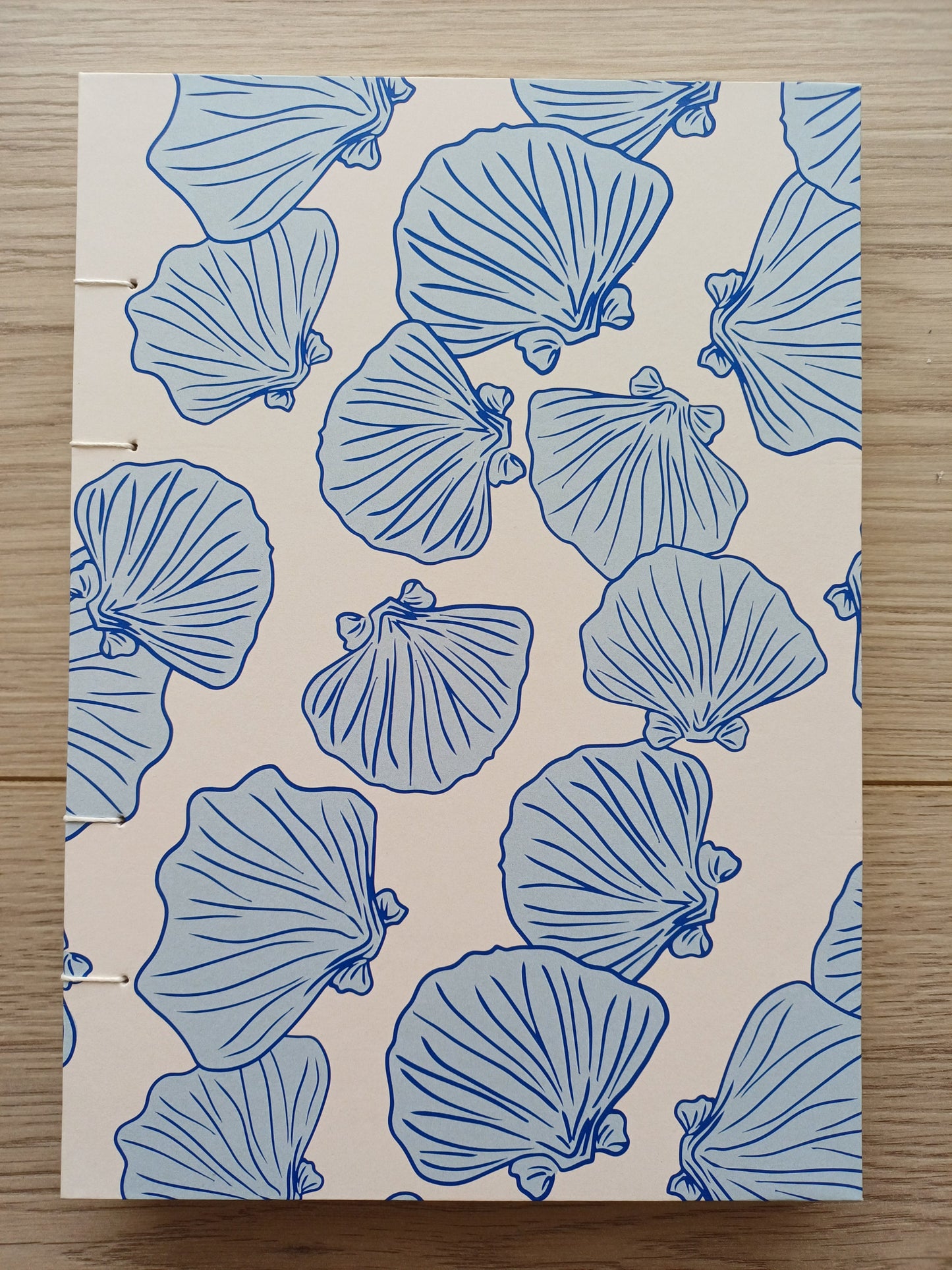 Couverture d'un carnet artisanal pour aquarelle avec des motifs de coquillages bleus sur un fond beige.