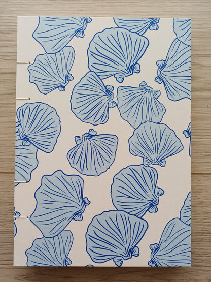 Couverture d'un carnet artisanal pour aquarelle avec des motifs de coquillages bleus sur un fond beige.