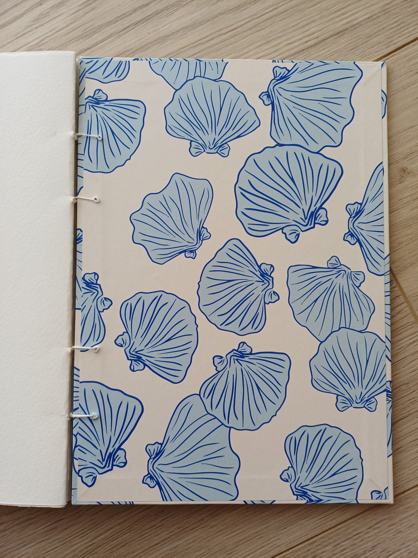Couverture d'un carnet artisanal pour aquarelle ouvert sur page de garde avec des motifs de coquillages bleus sur un fond beige.