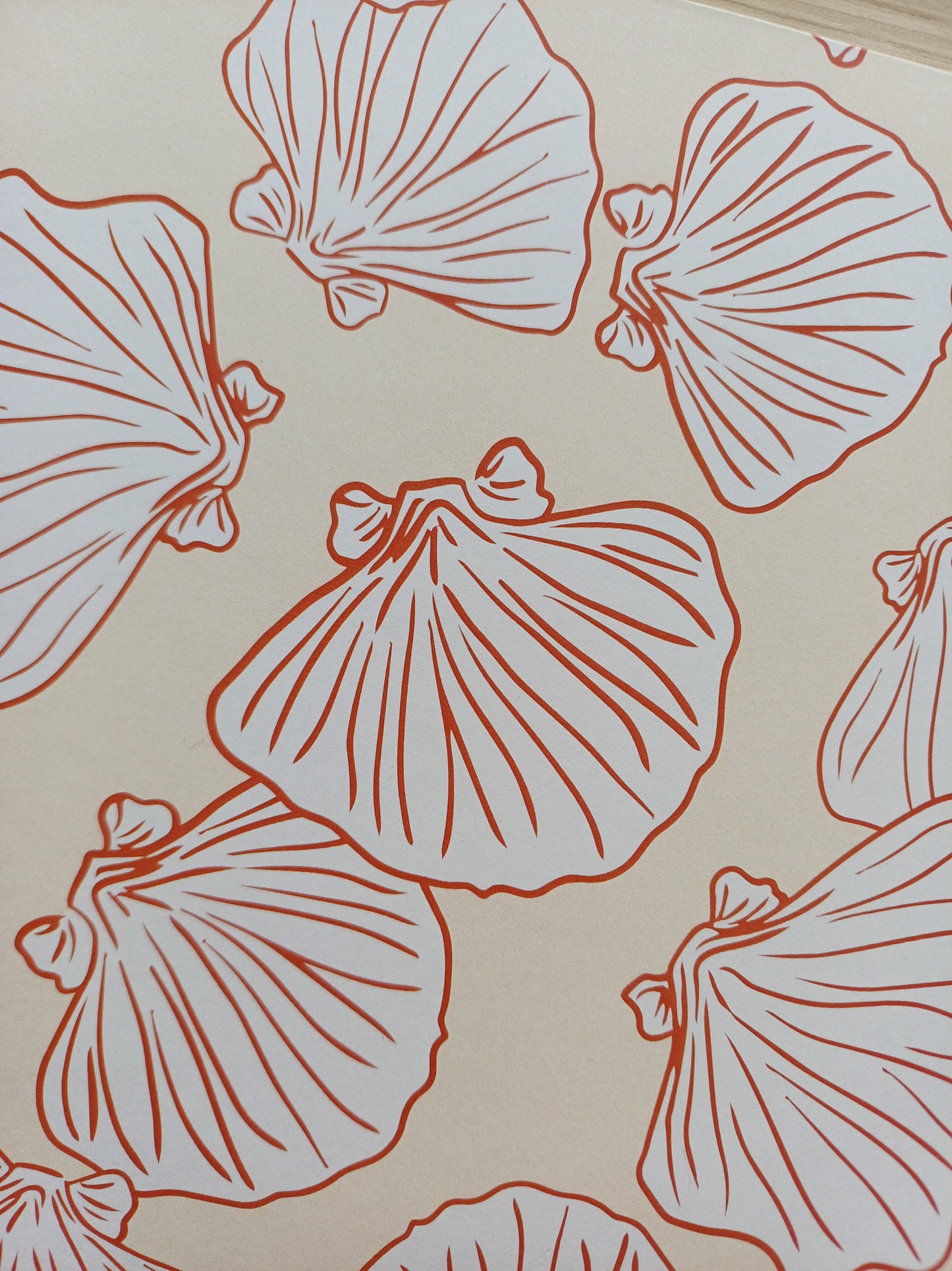 Détail de la couverture d'un carnet artisanal pour aquarelle avec des motifs de coquillages terracotta sur un fond beige.