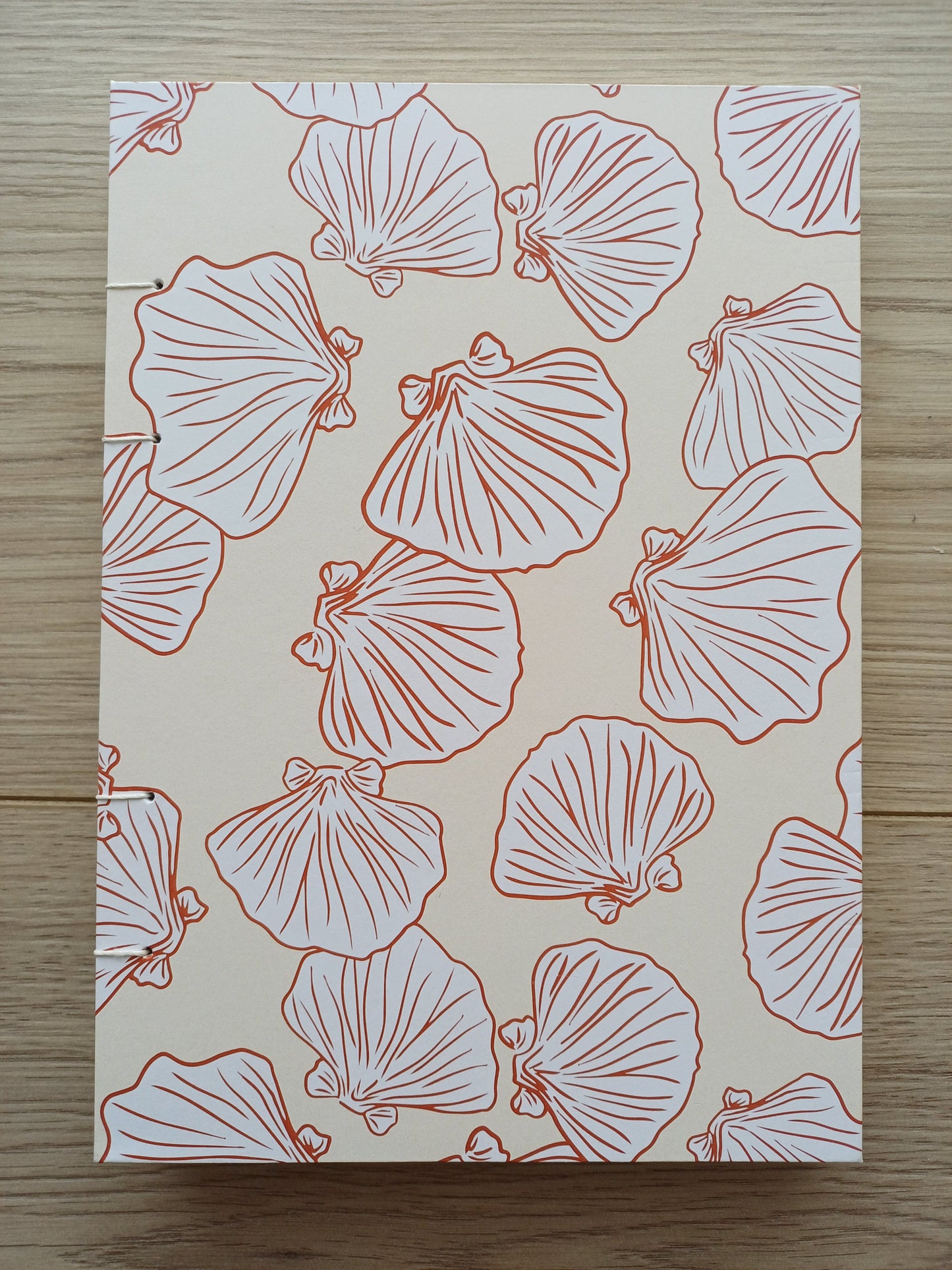 Couverture d'un carnet artisanal pour aquarelle avec des motifs de coquillages terracotta sur un fond beige.