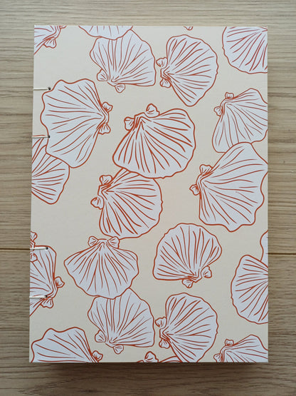Couverture d'un carnet artisanal pour aquarelle avec des motifs de coquillages terracotta sur un fond beige.