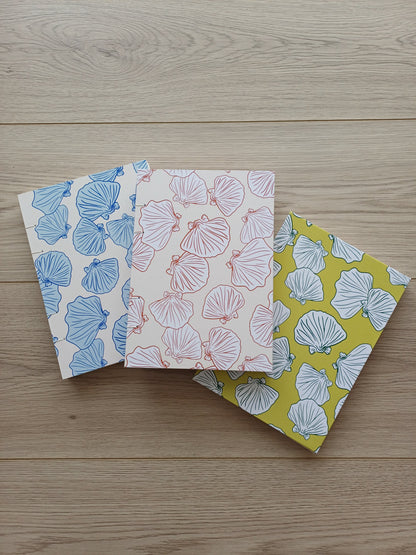 Couverture de trois carnets artisanaux pour aquarelle avec des motifs de coquillages sur des fonds vert, terracotta et bleu.